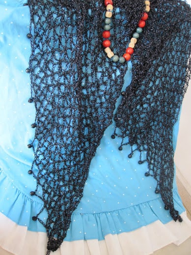 Black shawl draped over a light blue ruffled dress, styled with a colorful beaded necklace.