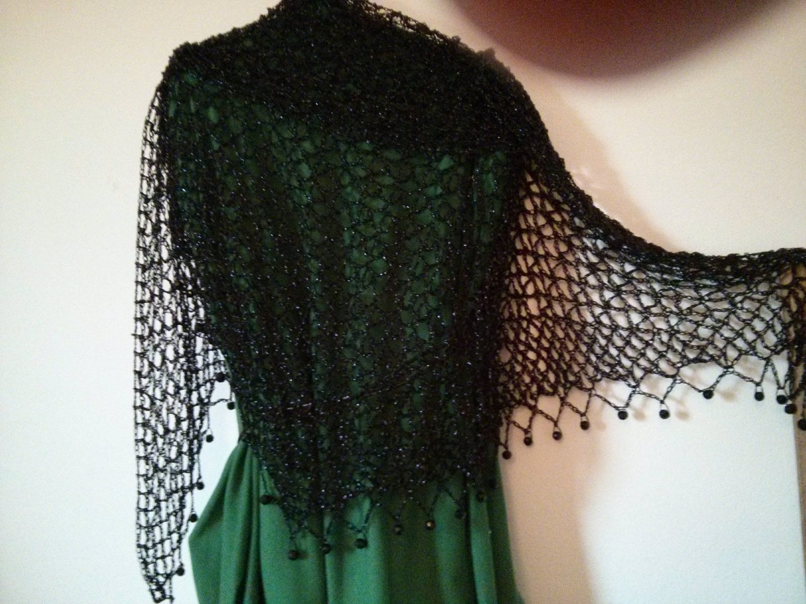 Black shawl draped over a green dress, back and side view of the openwork wrap.