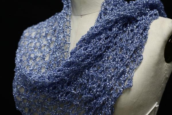 Blue lurex crochet shawl draped over a mannequin's shoulder, close side view of the shimmering openwork.
