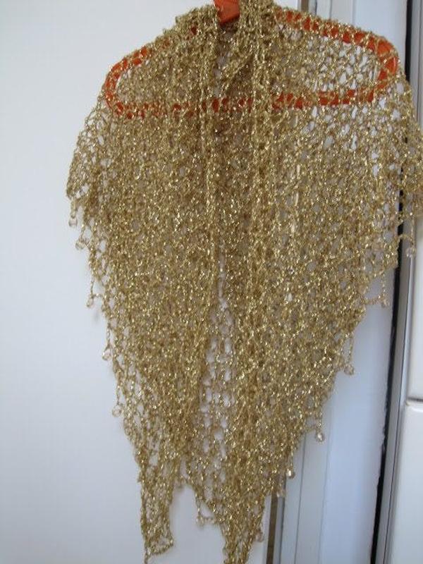 Champagne gold lurex shawl on an orange hanger against a white door, full-length view of the shimmering drape.