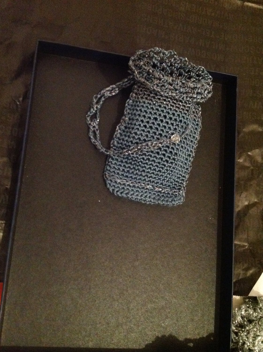 Grey crochet clutch bag resting in a dark gift box, top view of the shimmering evening handbag.