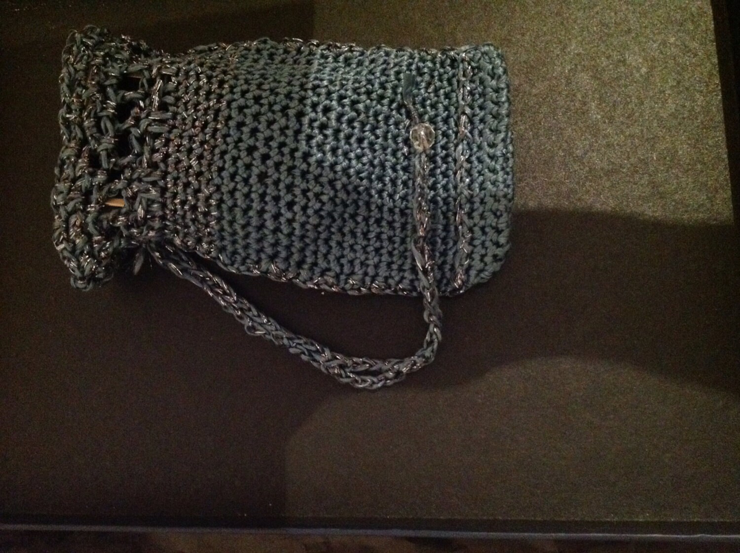 Grey crochet clutch bag from an alternate angle, showing the drawstring-style closure and strap.