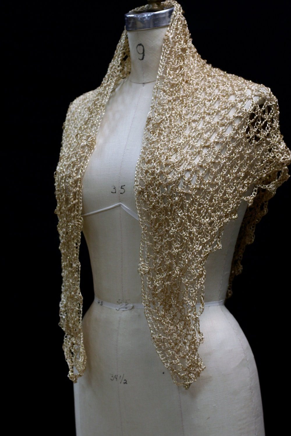 Gold beaded crochet shawl draped over a dress-form mannequin, front view of the shimmering wrap against a dark background.