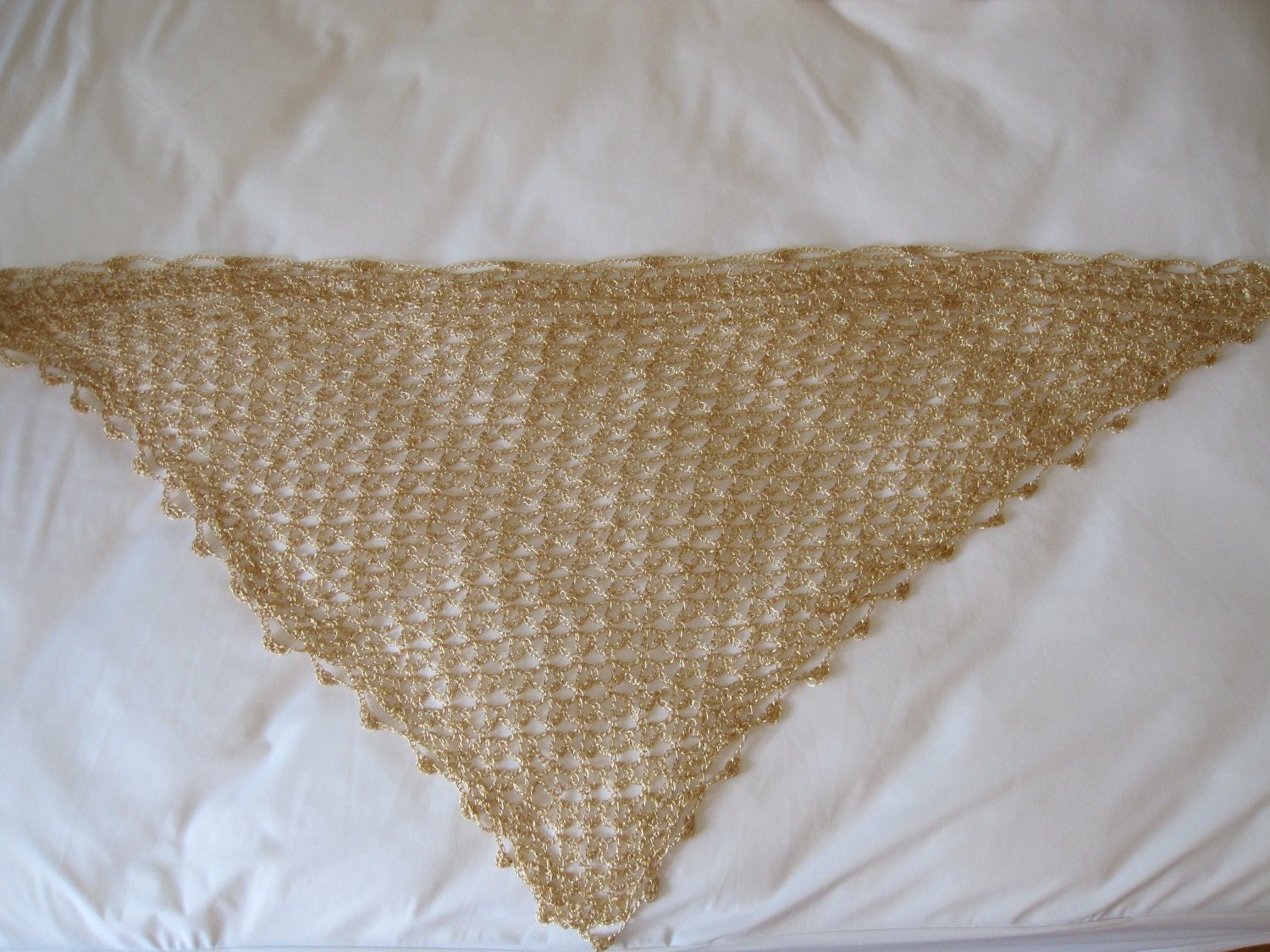 Flat lay of the gold lurex crochet shawl from a second angle, showing the pointed hem and delicate beadwork along the border.