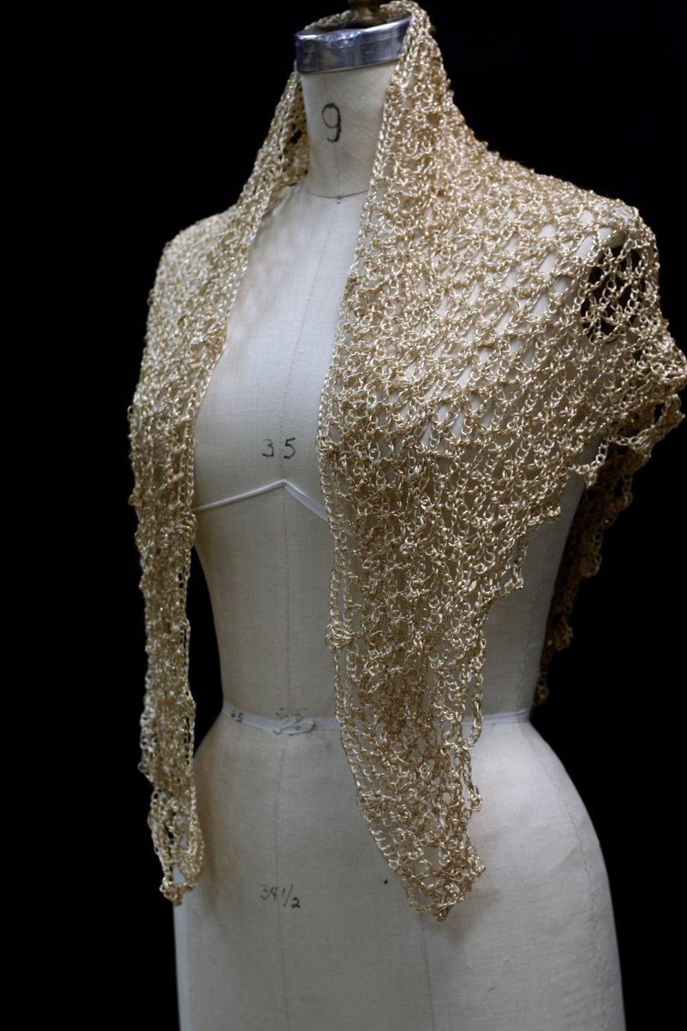 Gold beaded crochet shawl draped over a dress-form mannequin, front view of the shimmering wrap against a dark backdrop.