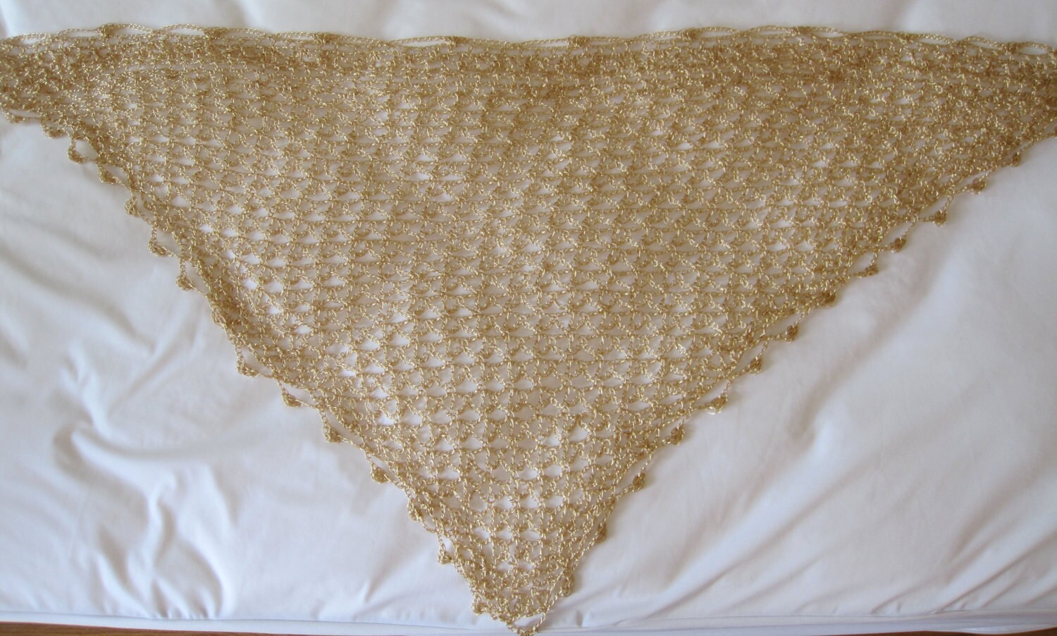 Gold beaded shawl laid flat in a triangle on a white surface, full view of the fine crochet and beaded border.