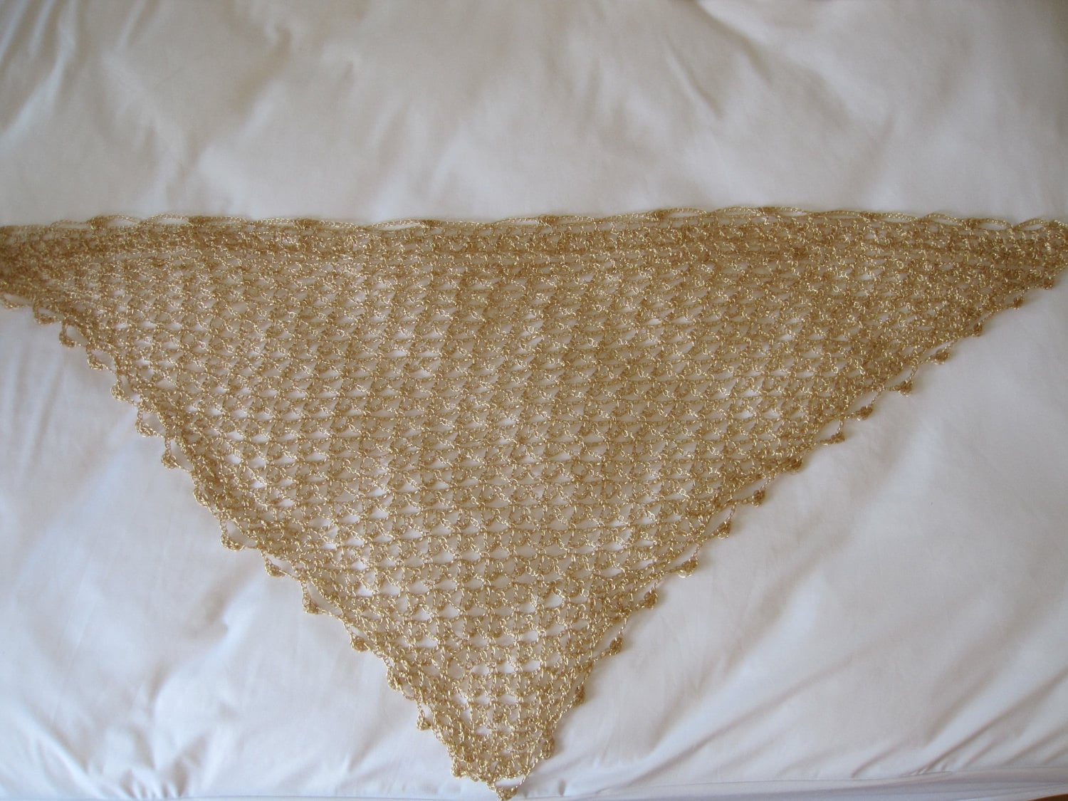 Flat lay of the gold crochet shawl from a second angle, showing the pointed hem and delicate beadwork.
