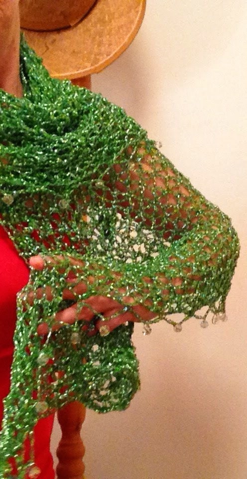 Green lurex shawl wrapped around the shoulders over a red dress, side view of the beaded openwork with a straw hat above.