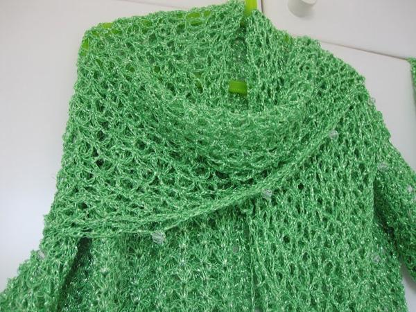Bright green lurex crochet shawl hanging in a soft cowl fold, close view of the openwork stitches.