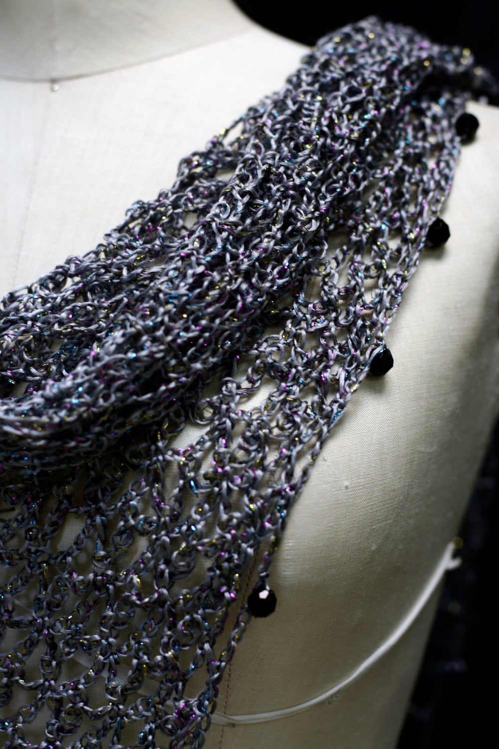 Close-up of the grey shawl's beaded edge on the mannequin, dark beads hanging from the scalloped trim.