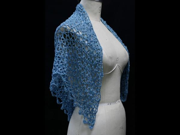 Light blue lurex crochet shawl draped over a mannequin's shoulder, side view of the delicate openwork.