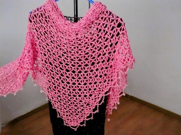 Pink lurex crochet shawl on a hanger over a black dress, full view of the shimmering openwork wrap.