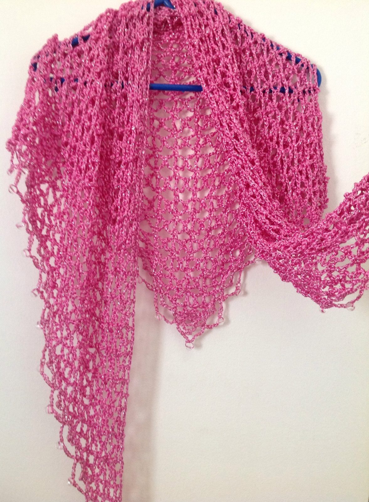 Pink shawl hanging with one end extended, showing how the lightweight crochet drapes.