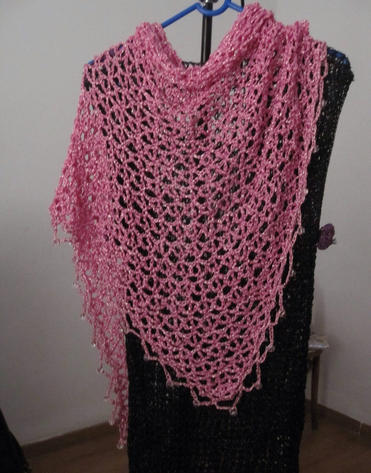 Pink lurex shawl on a hanger over a black dress, front view of the beaded openwork.