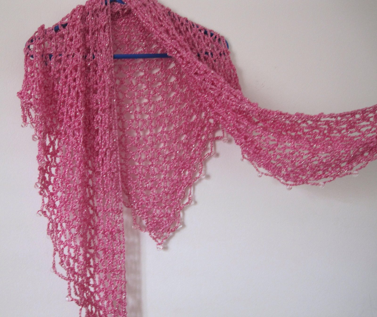 Pink shawl on a hanger with one end draped long, view of the flowing beaded trim.