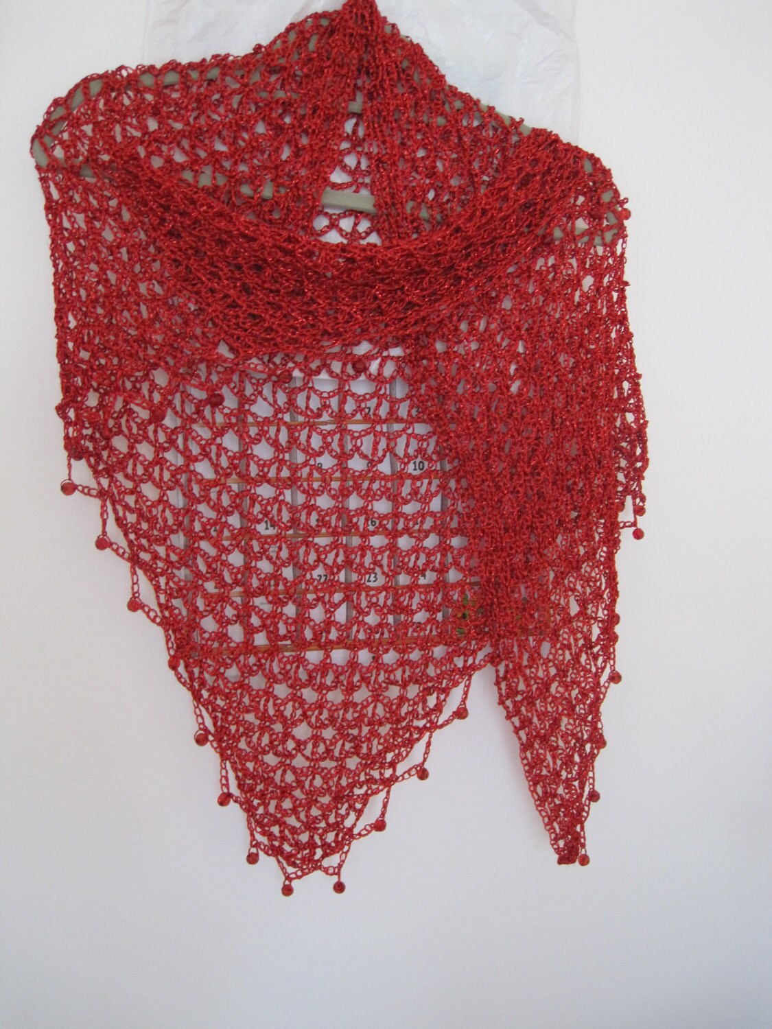Red shawl hanging flat, full triangle view of the openwork pattern with beaded points along the hem.