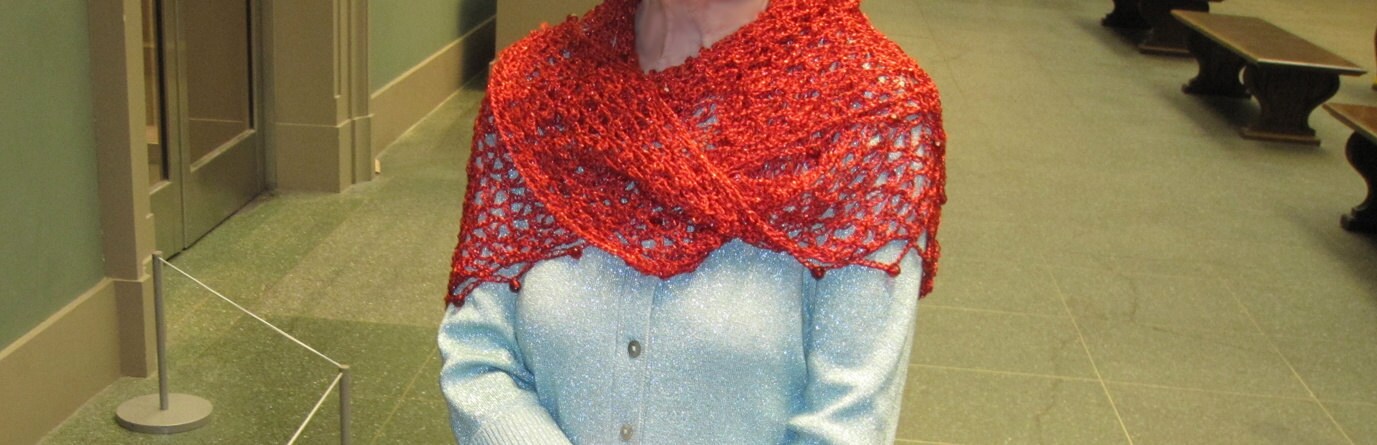 Red shawl worn as a shoulder wrap over a light blue top, photographed in an indoor lobby setting.