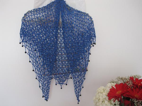 Sapphire blue lurex shawl hanging in a full drape, dark beads along the edge, flowers arranged below.