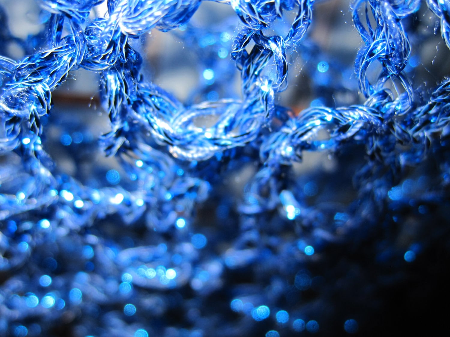 Extreme close-up of the sapphire lurex crochet, glittering blue stitches in fine detail.