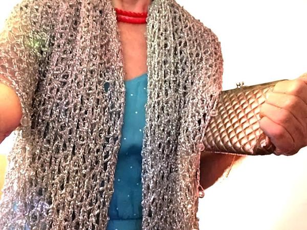 Woman wearing a silver lurex crochet shawl over a turquoise dress with a red necklace, holding a metallic clutch as the wrap frames her shoulders.