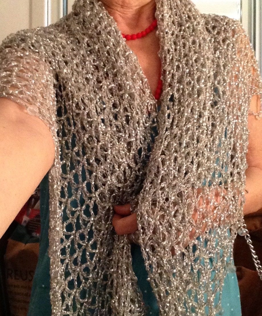 Front view of the silver crocheted lurex shawl draped over a turquoise dress, one hand resting at the waist, showing the open stitchwork.