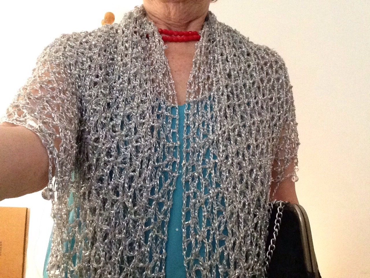 Silver lurex crochet shawl draped like a cape over a turquoise dress and red necklace, front view of the sparkling openwork.