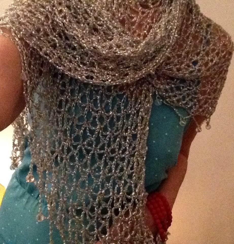 Woman in a turquoise dress wearing the silver crochet shawl around her shoulders, red bracelets at her wrist.