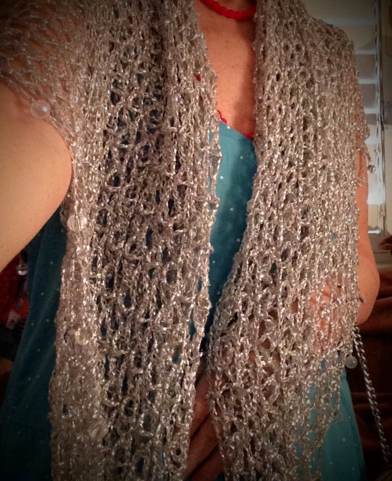 Silver crochet shawl draped over a turquoise dress, front view of the airy open stitches.