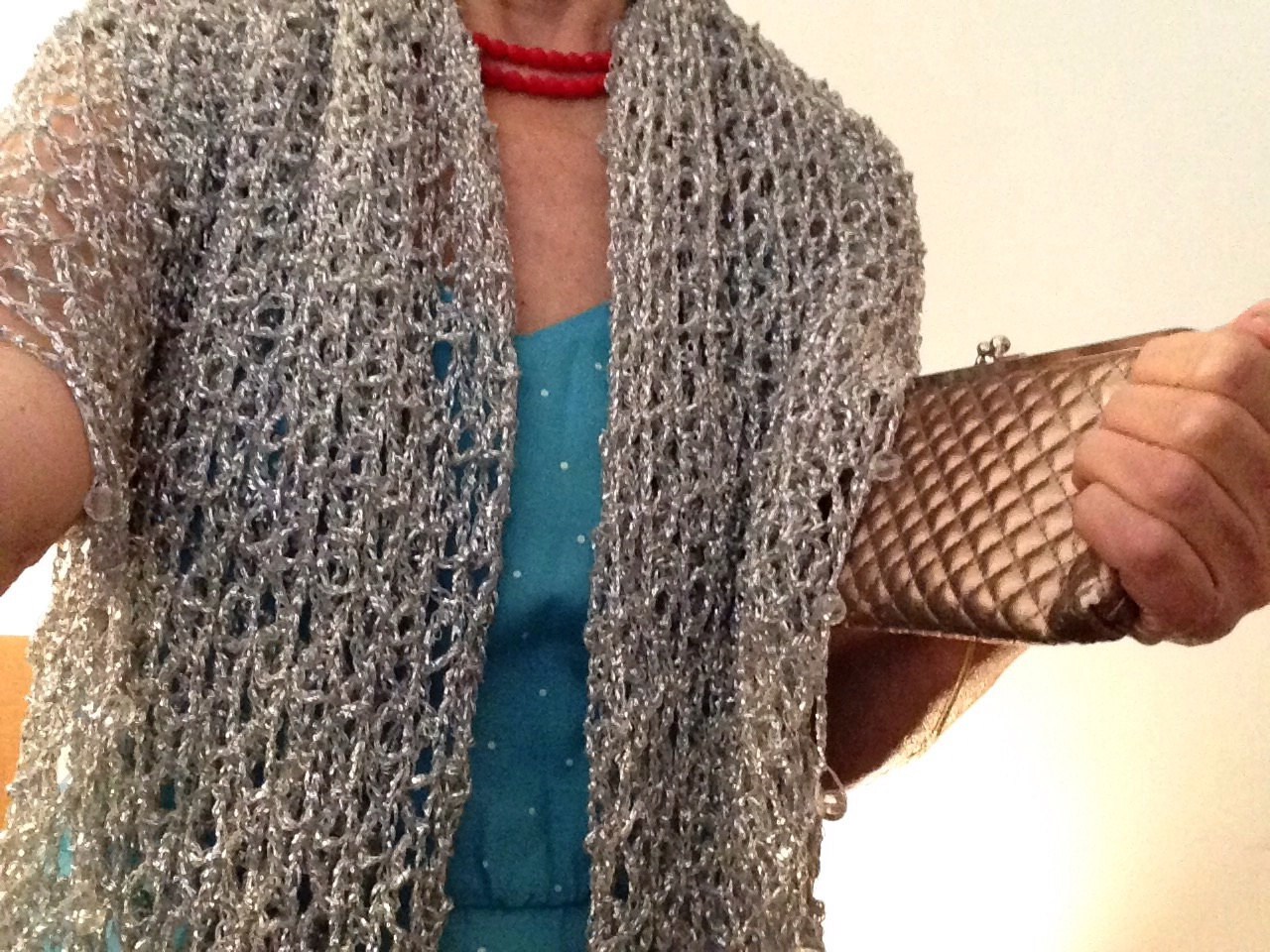 Woman in a turquoise dress with the silver shawl, holding a metallic clutch at her side.