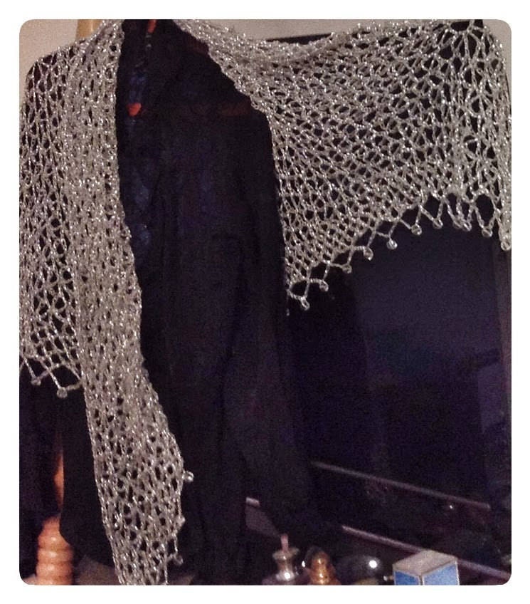 Silver beaded shawl draped over a black garment, side view highlighting its long, flowing openwork drape.