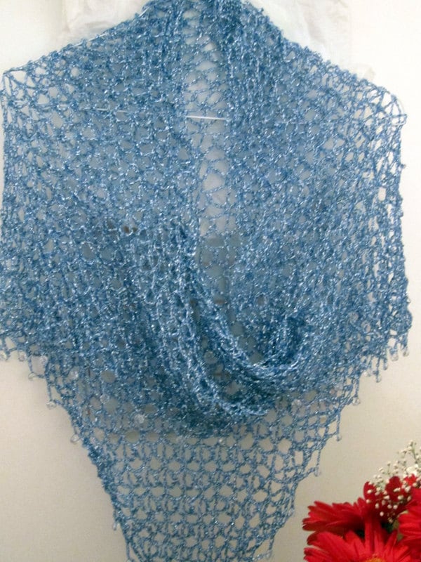 Sky blue shawl on a hanger folded into a soft cowl, red flowers arranged below.