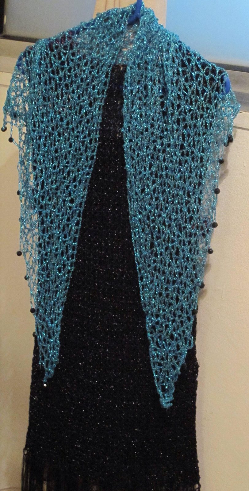 Turquoise shawl hanging straight over a black dress, symmetric front view of the sparkling wrap.