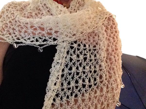 Ivory lurex shawl worn over the shoulders with a black top, close view of the openwork stitches.