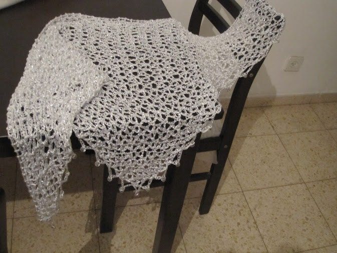 White shawl spread over a dark chair, full view of the airy openwork pattern.