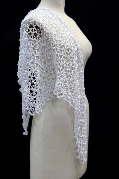 Side view of the white shawl on the mannequin, showing the openwork falling past the shoulder.