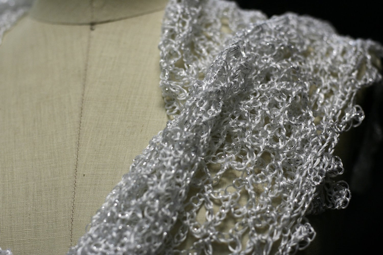 Close-up of the white lurex crochet on the mannequin's shoulder, fine stitches and subtle sheen.