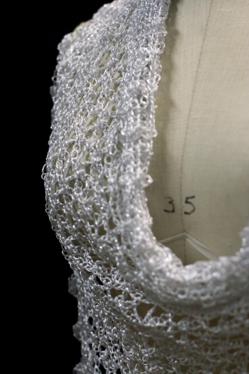 Close view of the white shawl's neckline drape on the mannequin, layered folds of openwork.
